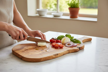 Hartekiste olive wood serving board with rustic edge and handle, being used to slice mozzarella and tomatoes.